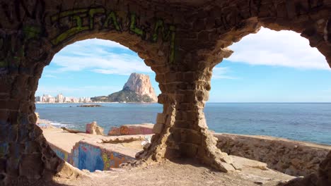 Vista-Por-Drones-De-La-Icónica-Montaña-Y-Costa-De-Calpe,-España,-Peñón-D&#39;ifach,-También-Conocido-Como-Roca-De-Calpe:-Vista-A-Través-De-Ventanas-Circulares-Pintadas-En-Un-Edificio-De-Graffiti-Abandonado