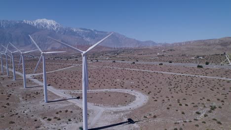 Drone-rotates-around-a-windmill,-revealing-a-line-of-working-windmills-in-the-desert