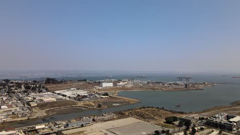 Vista-Soleada-Por-Drones-Del-Vecindario-Bayview-Con-Vista-A-La-Bahía-De-San-Francisco-Con-Barcos-De-Carga-Y-El-Horizonte-De-Oakland