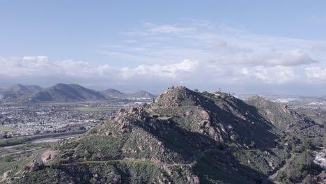 Drone-ascends-hill-in-Riverside,-California,-revealing-cross-at-summit