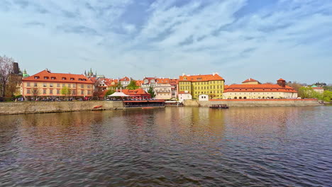 Wooden-boat-sailing-by-city-river-embankment-with-picturesque-houses