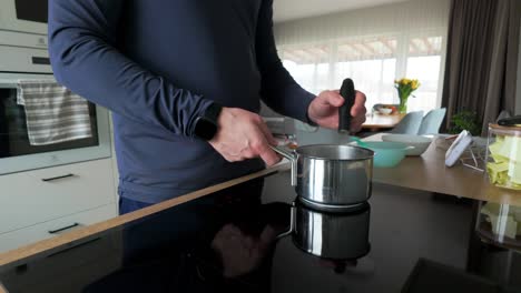 Shot-of-a-man-stirring-porridge-in-an-aluminum-pot-with-a-whisk-on-the-electric-stove-in-a-home-kitchen