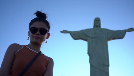 Una-Mujer-Con-Gafas-De-Sol-Posa-Con-Gracia-Junto-A-La-Impresionante-Vista-De-Cristo-Redentor-En-Río-De-Janeiro,-Contemplando-La-Magnificencia-De-Esta-Emblemática-Maravilla-Del-Mundo.