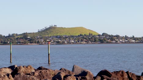 A-handheld-shot-of-Mangere-Mountain-volcano-across-the-bay-in-the-city-of-Auckland,-New-Zealand,-on-a-clear-and-blue-day