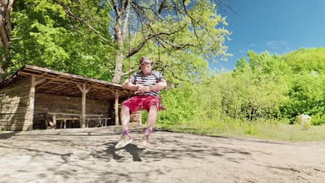 Elderly-man-enjoying-relaxing-mood-sits-on-woodland-swing-on-lovely-day