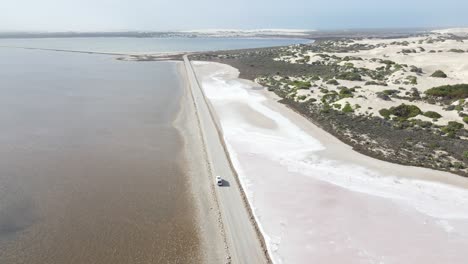 Drone-aerial-over-white-campervan-driving-on-road-over-pink-lake-MacDonnell-and-sand-dunes-in-South-Australia
