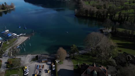 Drone-clip-showing-traditional-lake-side-Alpine-village-in-Switzerland,-with-harbour-and-snowy-mountains