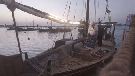 An-Emirati-fisher-man-collecting-shells,-and-pearl-extraction-on-a-wooden-old-boat-with-the-united-arab-emirates-flag-in-the-background,-A-boat-docked-with-a-fisherman-extracting-pearls-from-shells