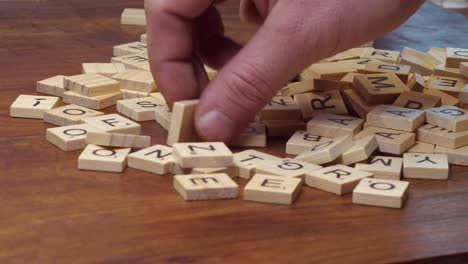 Man's-right-hand-flips-over-Scrabble-letter-tiles-on-wooden-table-top