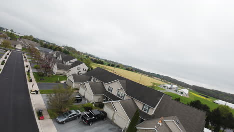 FPV-drone-flight-over-suburb-residential-area-with-Parking-cars,-agricultural-fields-and-baseball-court