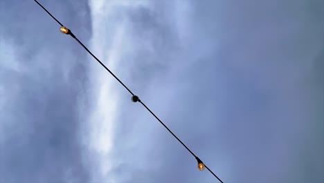 Glühbirnen-An-Einer-Lichterkette-Mit-Einer-Wolkenlandschaft-Im-Zeitraffer-Im-Hintergrund---Blick-Nach-Oben