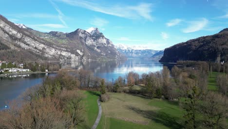 Drone-clip-of-calm-lake-surrounded-by-trees-and-snow-capped-mountains-in-the-Swiss-Alps