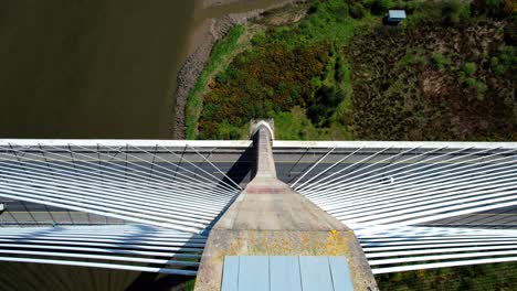 Drone-looking-down-cement-pylon-and-suspension-cables-to-bridge-deck-with-river-flowing-underneath-Thomas-Francis-Meagher-Bridge-in-Waterford-Ireland-impressive-project