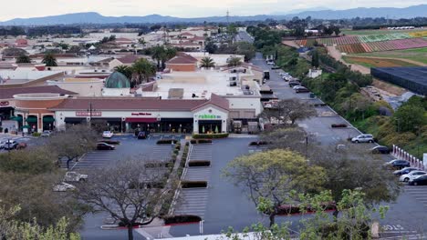 Movimiento-Hacia-Adelante-Vuelo-De-Drones-Carlsbad-Premium-Outlets-Al-Extremo-Sur-Del-Centro-Comercial-Campos-De-Flores-Al-Fondo-Lateral-Floración-Parcial-Rayas-Coloridas-Y-Estacionamiento-Verde-Visible