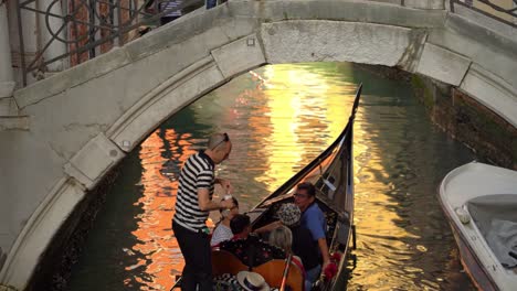 Gondolier-with-gondola-sails-a-couple-of-tourists-in-one-of-many-water-canals-in-Venice-on-a-warm-spring-day