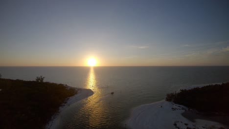 Aerial-4K-Drone-footage-of-the-sun-setting-and-reflecting-over-the-sea-off-Calm-Pass,-in-Naples,-Florida,-USA