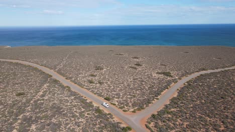 Drone-aerial-showing-a-van-driving-along-a-country-road-by-a-beautiful-blue-ocean