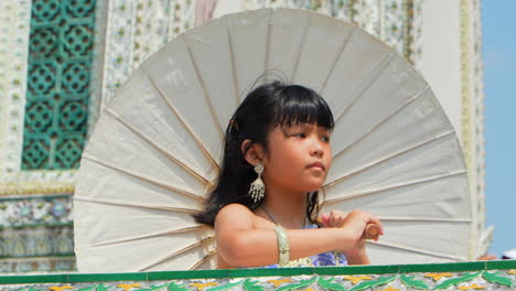 Süßes-Kleines-Thai-Mädchen-Bewegt-Ihren-Regenschirm-In-Einem-Tempel-In-Bangkok