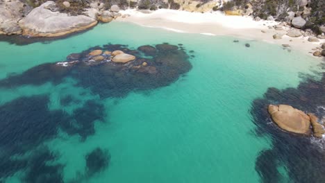 Drone-aerial-moving-towards-a-secluded-beach-with-blue-water-ands-white-sand-on-a-sunny-day