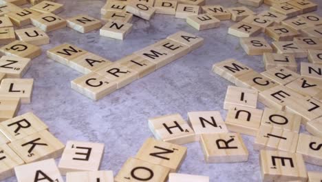 Closeup-fingers-form-Scrabble-crossword-with-CRIMEA-and-WAR-on-table