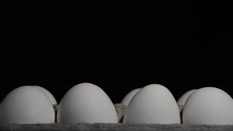 Tray-of-white-chicken-eggs-in-a-dark-room-being-lit-by-searching-flashlight,-close-up