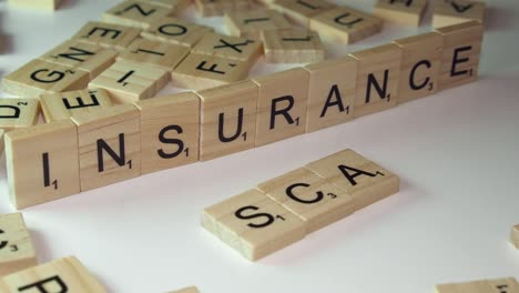 Hand-puts-Scrabble-tile-letters-on-table-to-form-words-INSURANCE,-SCAM