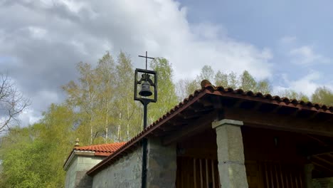 Wide-angle-pan-down-from-bell-and-cross-to-chapel-entrance-in-mountains