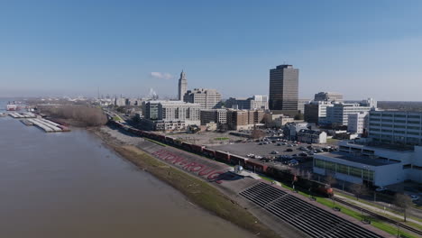 Wide-aerial-footage-of-the-Baton-Rouge-sign-on-the-banks-of-the-Mississippi-River-with-downtown-in-the-background-and-a-train-moving-by-the-sign