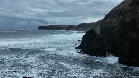 Right-to-left-drone-shot-of-waves-crashing-against-cliffs