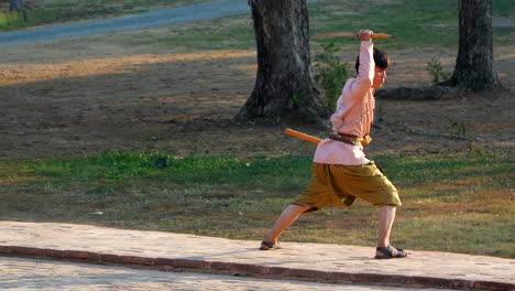 Chico-Con-Uniforme-Tailandés-Practicando-Movimientos-De-Katana.