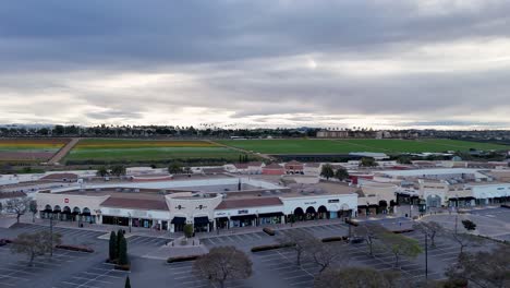 Vuelo-Con-Drones-Carlsbad-Premium-Outlets-Que-Cubren-La-Esquina-Noroeste-Del-Centro-Comercial-Moviéndose-Hacia-El-Extremo-Norte-Campos-De-Flores-Fondo-Floración-Parcial-Rayas-Coloridas-Y-Verde