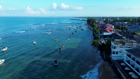 Aerial-drone-landscape-pan-of-charter-boats-docked-in-bay-near-main-street-with-hotel-restaurants-of-Turtle-Beach-Hikkaduwa-Sri-Lanka-Asia-travel-holidays