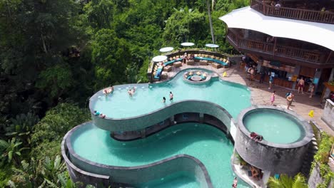 People-relaxing-at-Multi-Level-Pool-of-Cretya-Jungle-Day-Club,-Drone-View