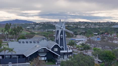 Carlsbad-Windmill-Teilweise-Kreisförmigen-Drohnenflug-Direkt-Vor-Uns,-Bewegung-Von-Links-Nach-Rechts-Mit-Parallax-Effekt-Straße,-Häuser-Und-Hotel-Im-Hintergrund