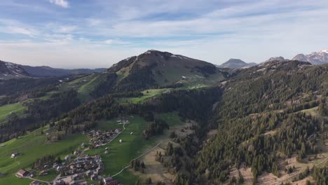 La-Belleza-De-La-Vida-Rural-Con-Estas-Imágenes-De-Drones-Que-Capturan-Majestuosas-Montañas,-árboles-Altos,-Pasto-Verde-Y-El-Encanto-De-Un-Pueblo-Ubicado-Bajo-Un-Cielo-Azul-Adornado-Con-Esponjosas-Nubes-Blancas-En-Amden-Sentis-Schweiz.