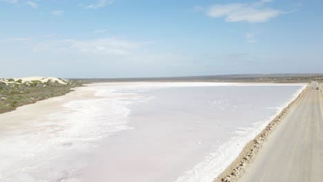 Drone-aerial-moving-forward-over-pink-lake-MacDonnell-and-sand-dunes-in-South-Australia