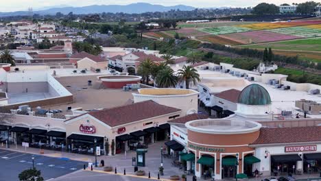 Vorwärtsbewegung-Drohnenflug-Carlsbad-Premium-Outlets-Zum-Südwestlichen-Ende-Des-Einkaufszentrums-Blumenfelder-Dahinter-Im-Hintergrund-Teilweise-Blühende-Bunte-Streifen-Parkplatz-Sichtbar