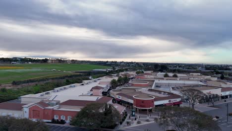 Vuelo-Con-Drones-Carlsbad-Premium-Outlets-Que-Cubren-El-Extremo-Norte-Del-Centro-Comercial-Campos-De-Flores-Al-Fondo-Lateral-Floración-Parcial-Rayas-Coloridas-Y-Verdes