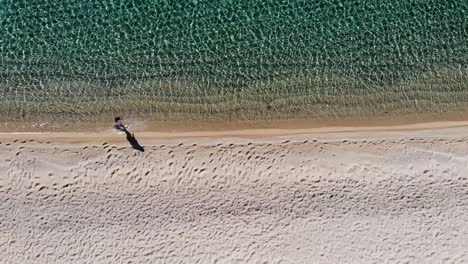 Mujer-Caminando-En-Aguas-Poco-Profundas-A-Lo-Largo-De-Una-Playa-Filmada-Con-Un-Dron