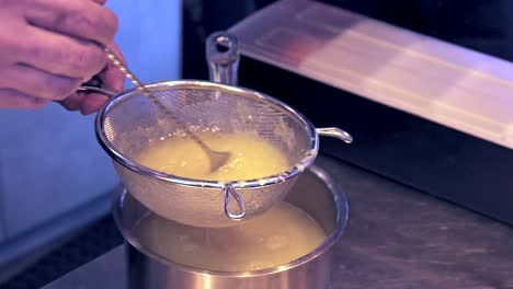 Close-up-side-view-of-bartender-stirring-lemon-juice-in-a-colander,-Slow-motion-100fps