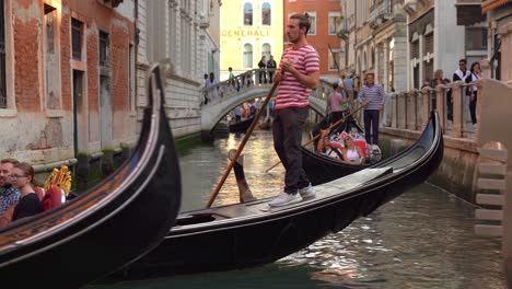 Young-Venetian-Gondolier-Sails-a-Group-of-Tourists-in-water-canal-in-Venice-on-a-Sunny-Day-in-Spring