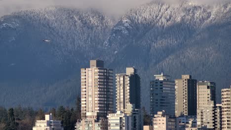 Airplane-Flying-Over-Coastal-Cityscape-And-Winter-Forest-Mountains-In-Vancouver,-British-Columbia,-Canada