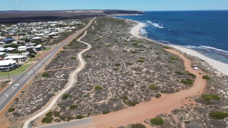 Drone-aerial-showing-a-country-road-next-to-a-blue-beach-in-Australia