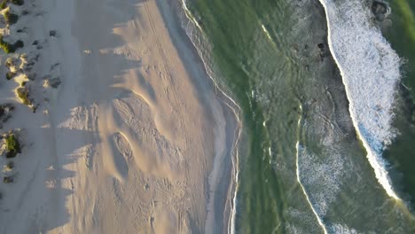 Drone-aerial-spinning-down-to-a-pristine-blue-beach-during-sunrise