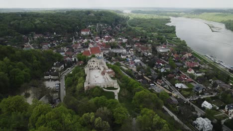 Aerial-panoramic-above-Kazimierz-Dolny-small-historic-town-Poland-Vistula-river-city-around-green-forested-area,-houses,-skyline-background