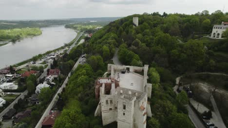 Drone-Fly-Renaissance-Castle-in-Kazimierz-Dolny-Town-Poland-Travel-Destination,-Aerial-view-of-forested-area-River-Vistula-and-buildings