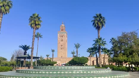 Historical-sandstone-tower-in-Morocco-between-palm-trees-in-strong-sun-and-balmy-sky