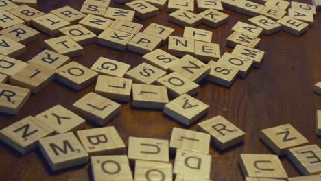 Dolly-Shot-Se-Arquea-Suavemente-Pasando-Por-Una-Variedad-De-Fichas-De-Juegos-De-Scrabble-En-Una-Mesa-De-Madera