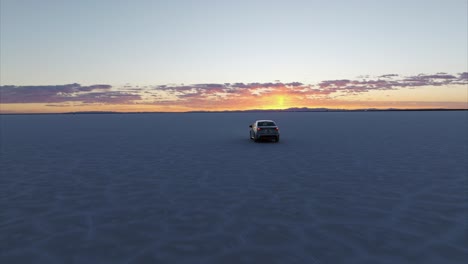 Driving-car-over-cracked-surface-of-salt-flats-in-Utah,-Aerial-tracking-and-sky-for-copy-space