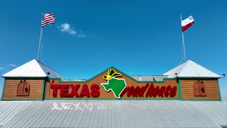 Waving-flag-of-USA-on-roof-of-Texas-Road-House-Restaurant-against-blue-sky